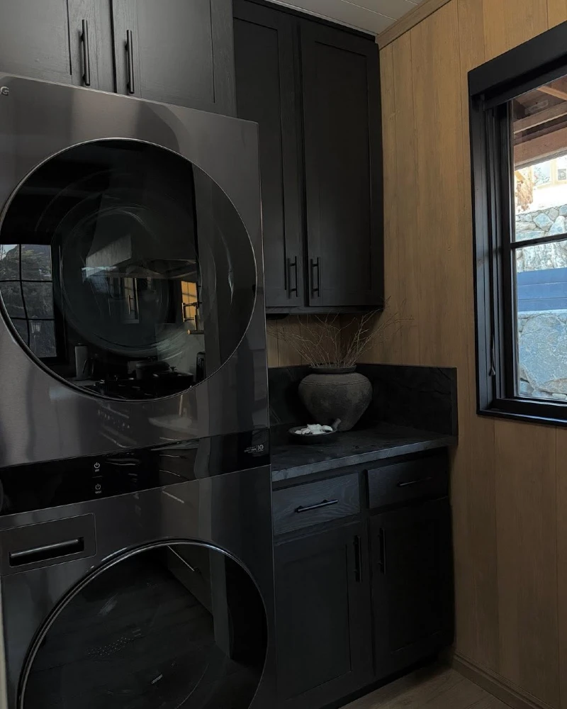 10. Charcoal Laundry Corner with Black Cabinets, Wood Panel Walls, and Stone Counter