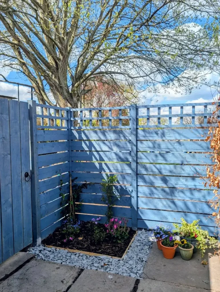 10. Soft Blue Slatted Fence with Corner Flower Bed and White Gravel Edge