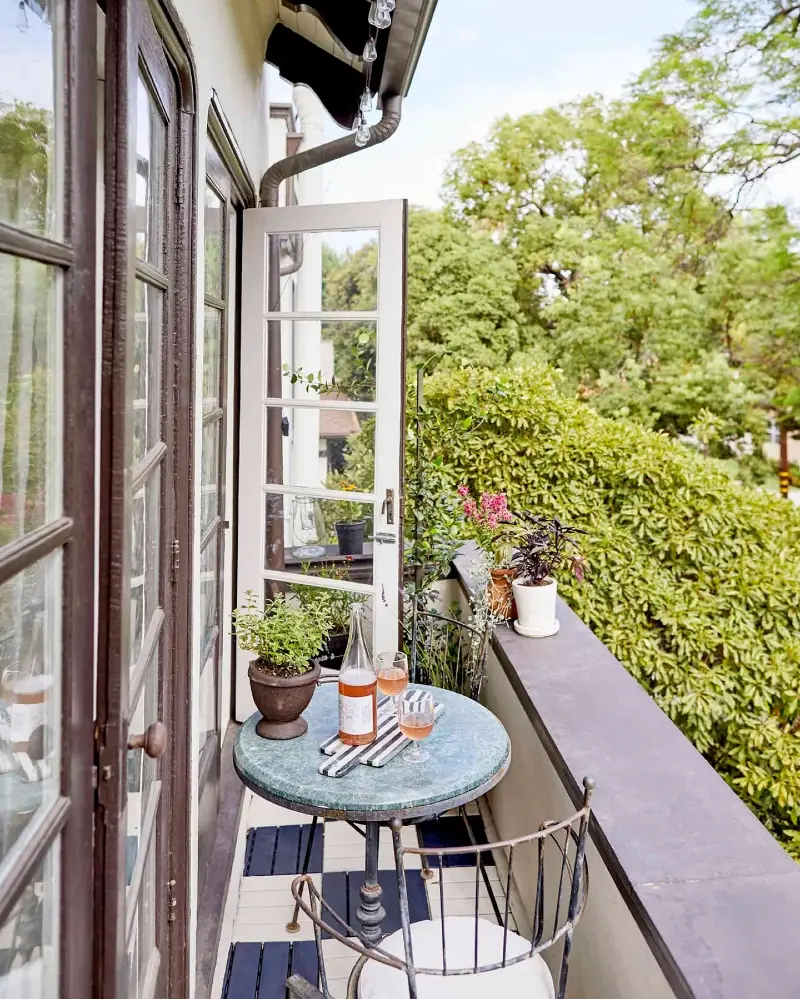10. Vintage Bistro Balcony with Patina Round Table, Open French Door, and Lush Green View
