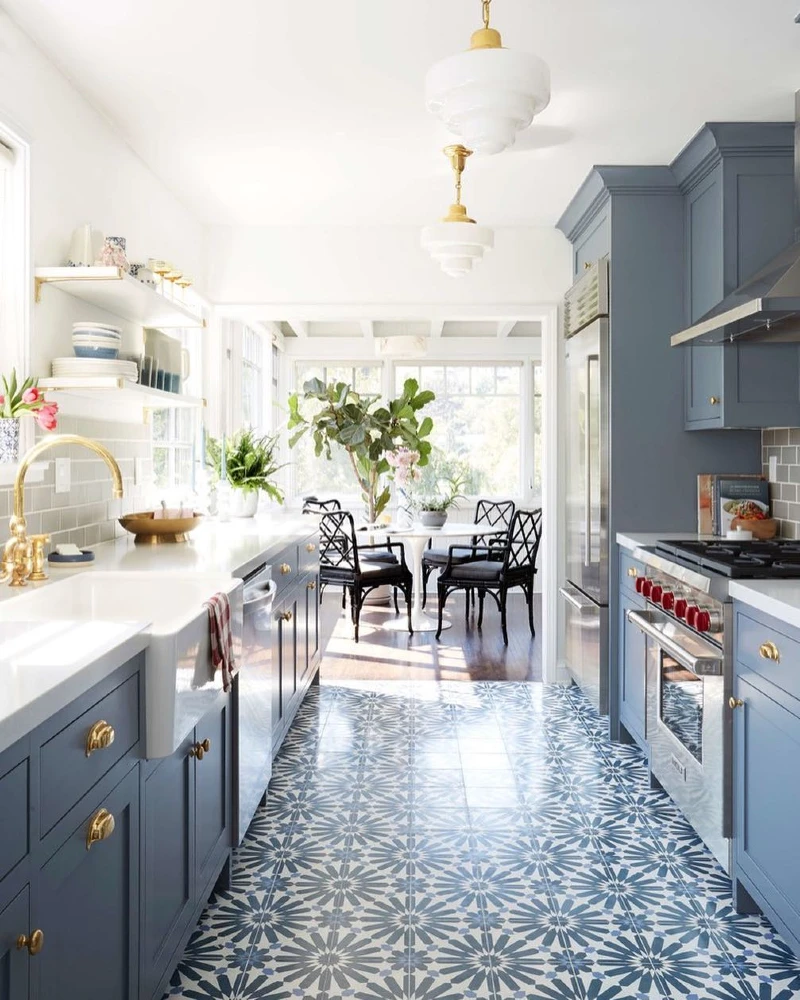 12. Blue Galley Kitchen with Brass Hardware, Patterned Tile Floor, and Sunlit Dining Nook