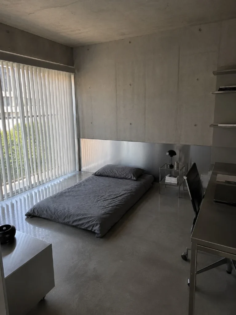 12. Floor Mattress with Concrete Walls, Metal Desk, and Vertical Blinds