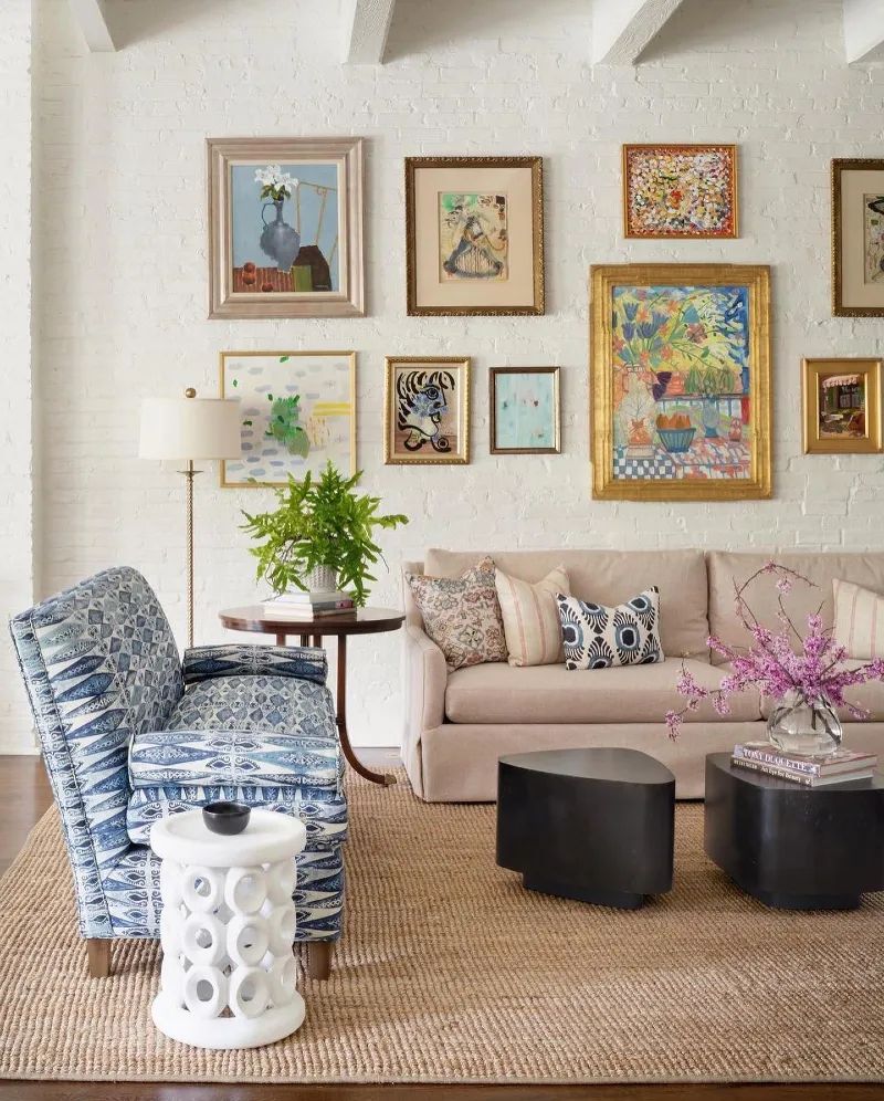 12. White Brick Gallery Wall with Gilded Frames and Color-Rich Art Above Neutral Sofa