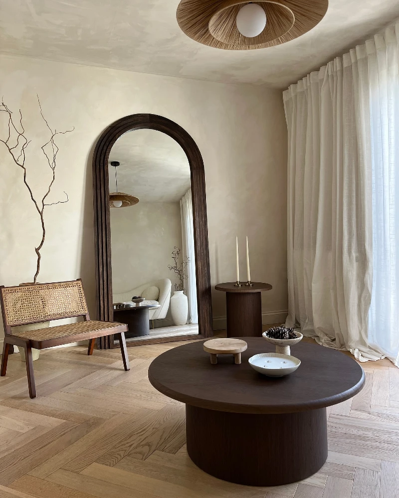 13. Arched Dark Wood Mirror with Round Coffee Table, Cane Bench, and Sheer Curtains