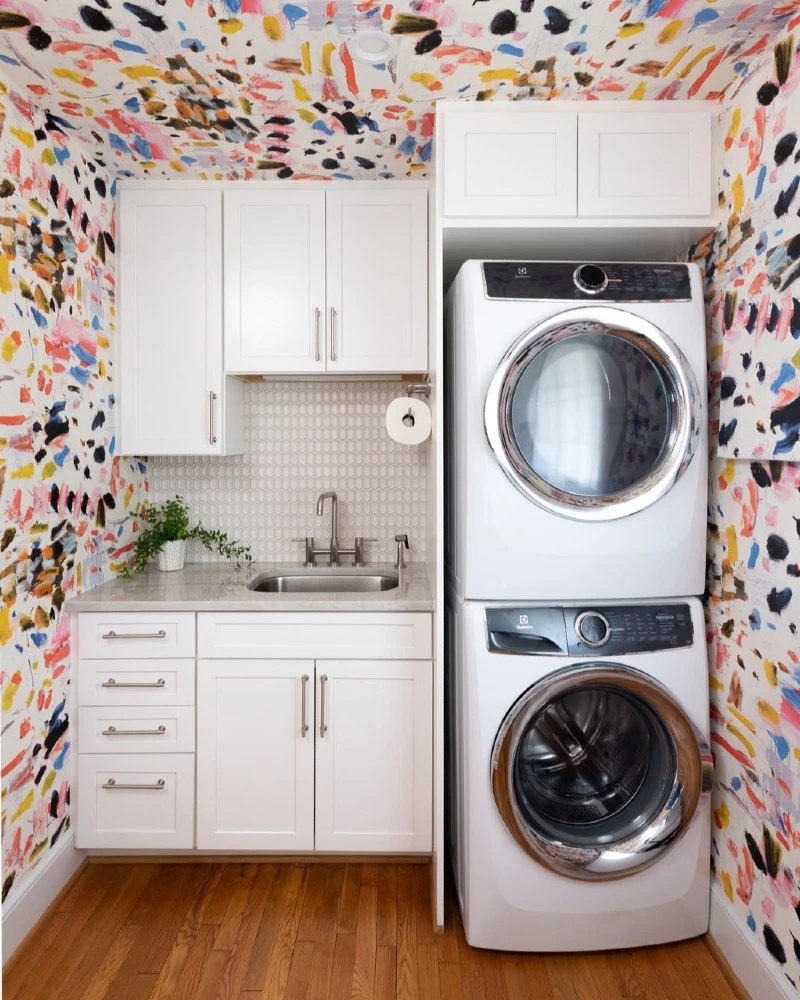 15. Maximalist Laundry Closet with Painted Wallpaper, White Cabinets, and Stacked Machines