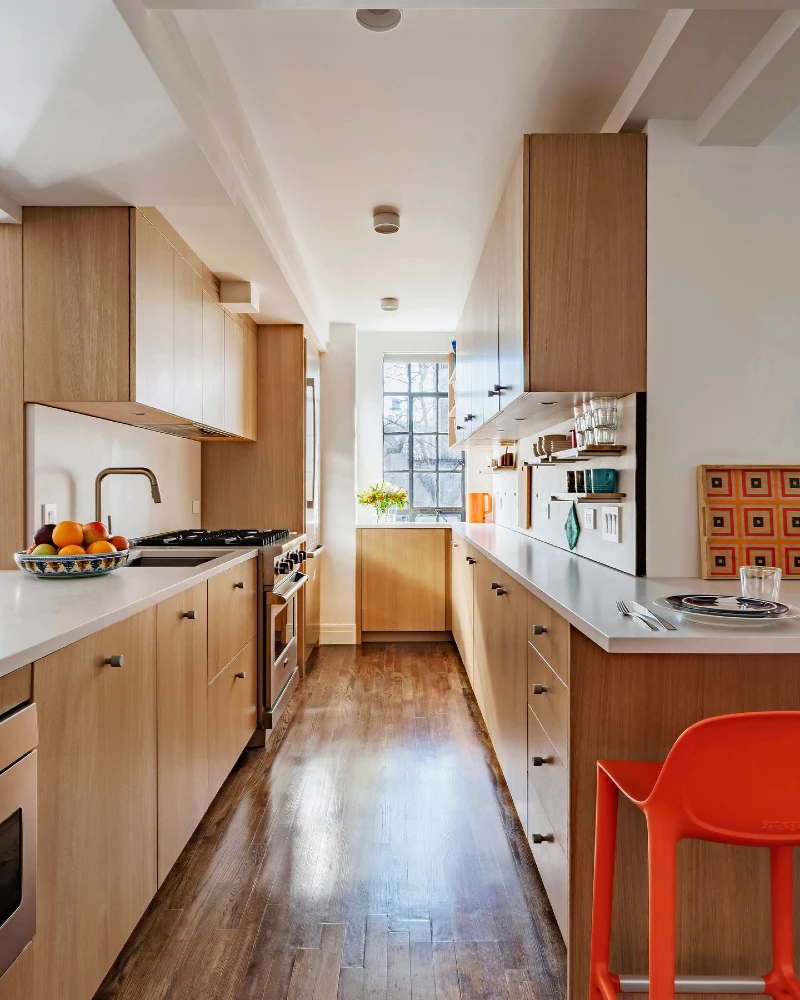 16. Light Oak Galley Kitchen with White Counters, Mini Open Shelves, and an Orange Chair