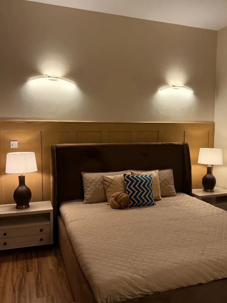 17. Tan Paneled Wall with Brown Wingback Headboard and Warm Double Lighting