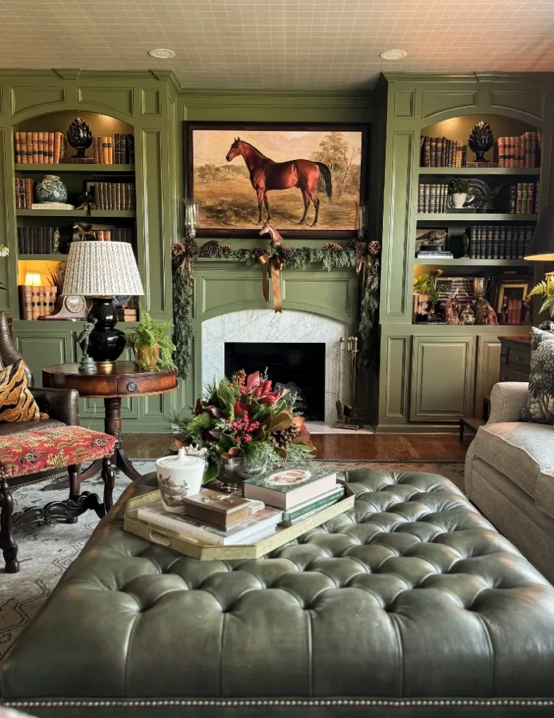 18. Olive Built In Bookcases with Horse Painting, Tufted Leather Ottoman, and Garland Mantel