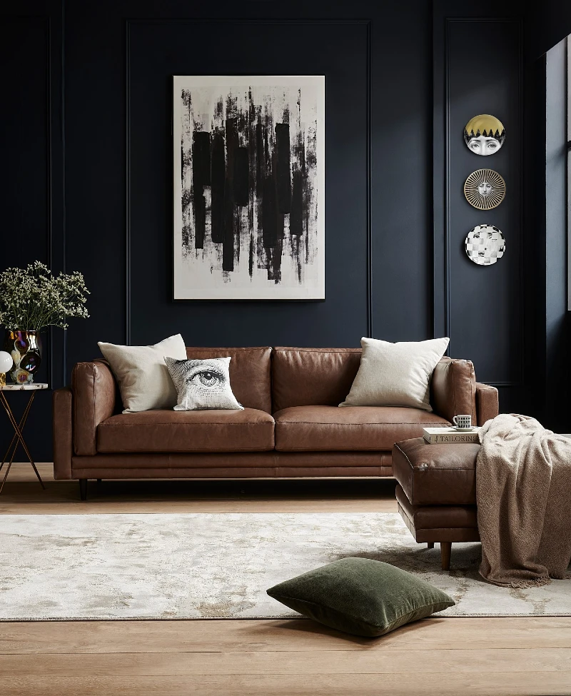 2. Cognac Leather Sofa with Black Paneled Walls and a Pale Oversized Rug