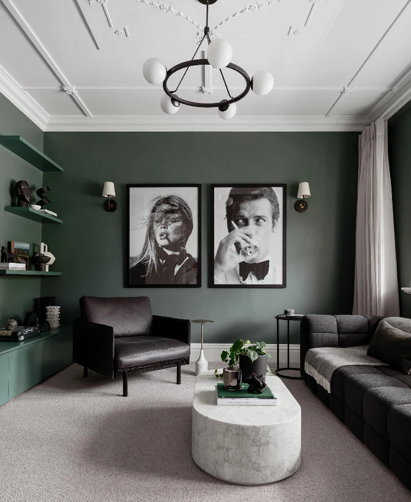 3. Forest Green Walls with Black Portrait Art and a Marble Drum Table