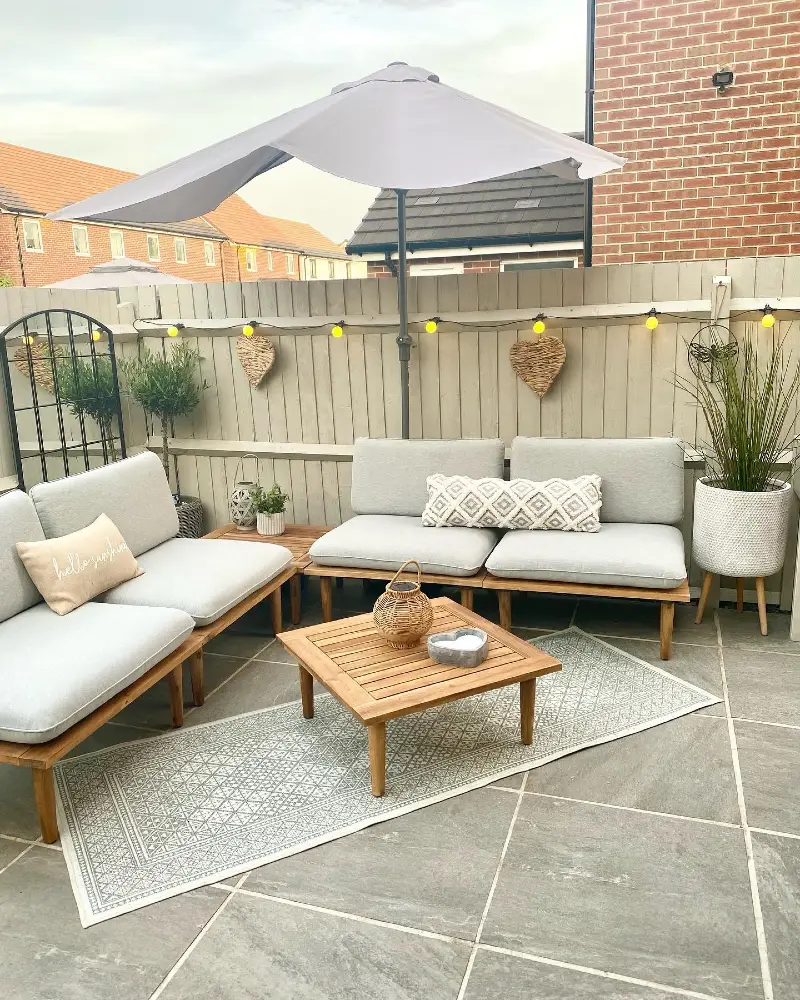 3. Pale Fence Patio with Globe Lights, Woven Hearts, and Grey Lounge Seating