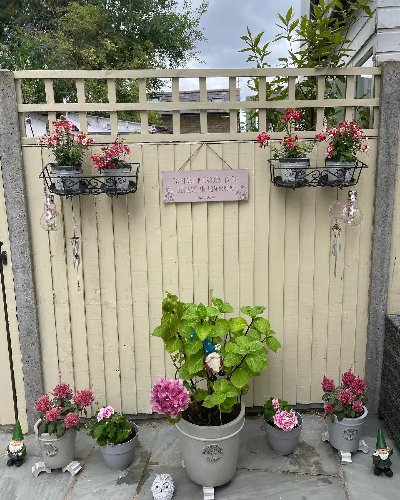 5. Cream Fence with Black Basket Planters, Pink Blooms, and Garden Sign