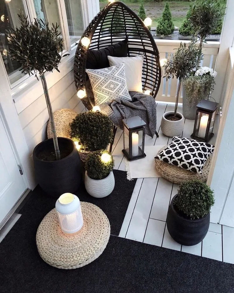6. Woven Egg Chair Balcony with Olive Trees, Lanterns, and Black Outdoor Rugs