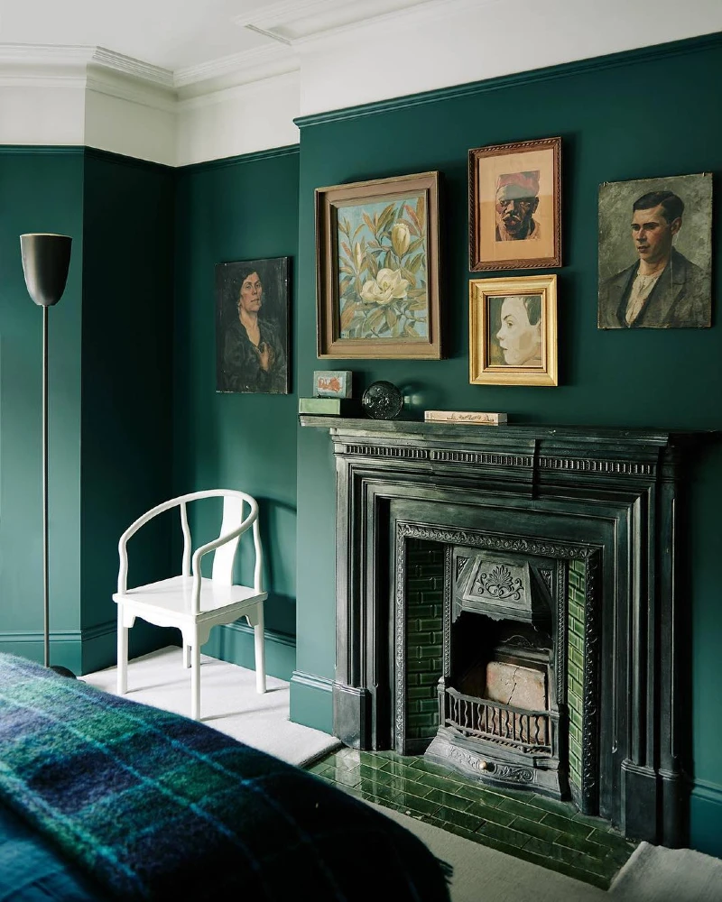 7. Dark Green Fireplace Wall with Vintage Portraits and a White Accent Chair