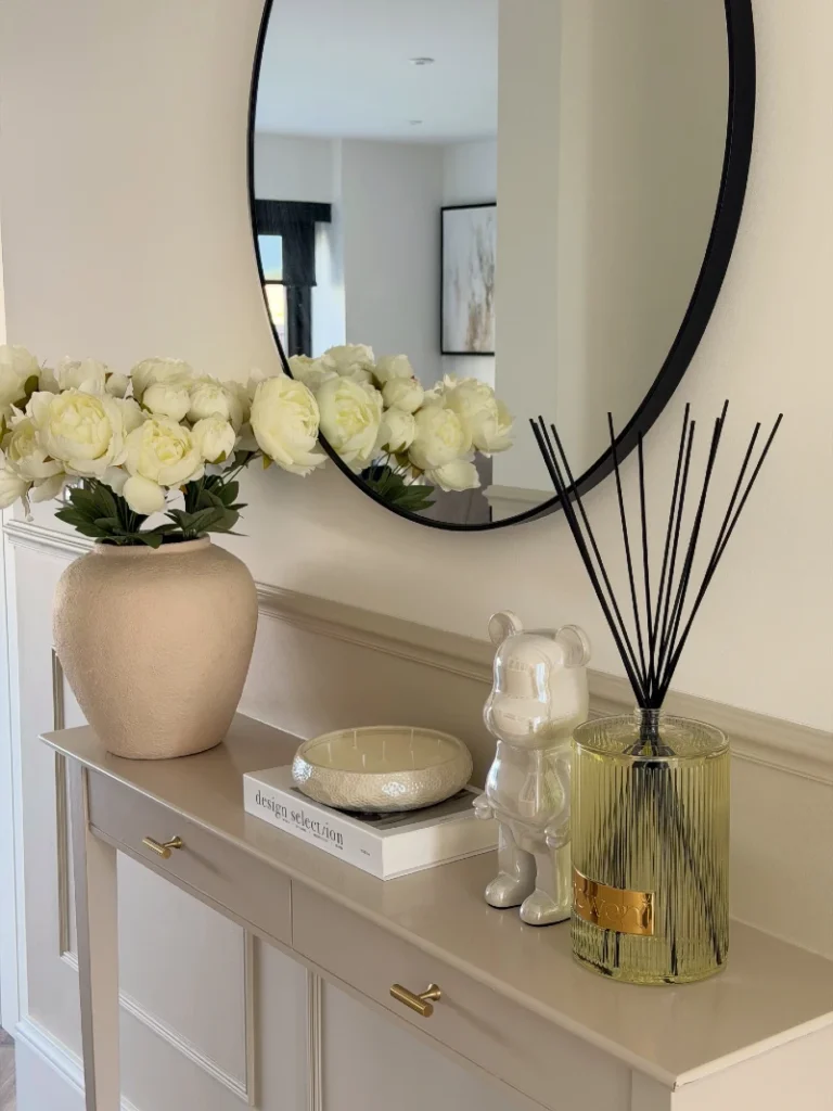 7. Round Black Mirror Above a Taupe Console with Cream Peonies and Reed Diffuser