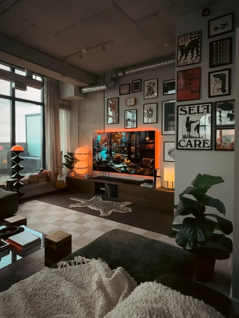 8. Moody Loft TV Wall with Graphic Prints, Orange Lamps, and Concrete Ceiling
