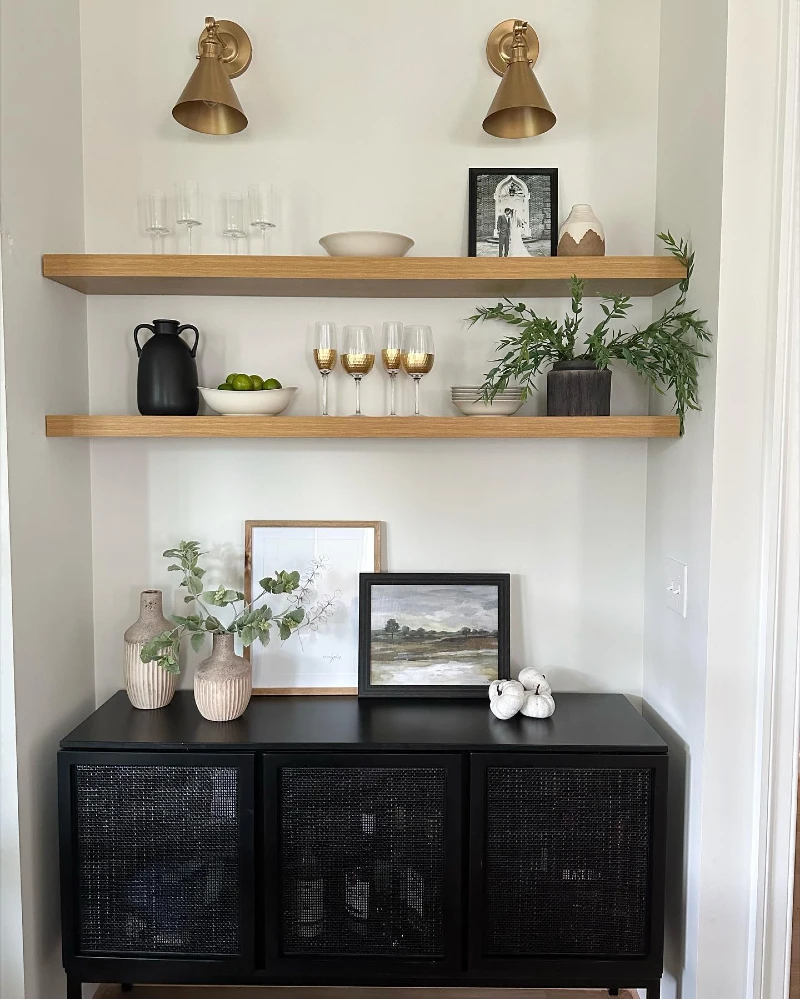 9. Black Cane Cabinet with Oak Shelves, Brass Sconces, and Trailing Greenery