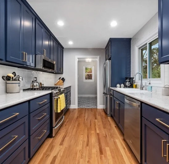 9. Navy Blue Galley Kitchen with Brass Pulls, White Counters, and Warm Wood Floors