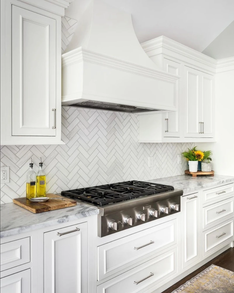 Classic White Herringbone Backsplash with Ornate Range Hood and Bright Minimal Cabinetry