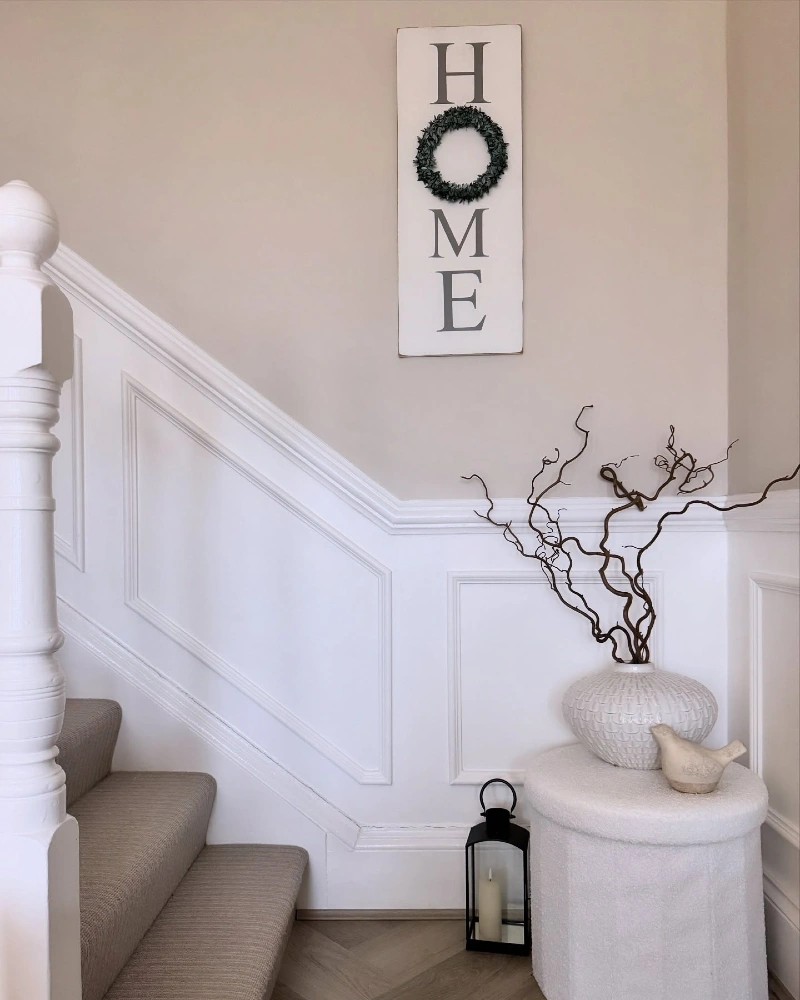 Crisp White Wainscoting with a Bouclรฉ Ottoman and Vertical Farmhouse Sign