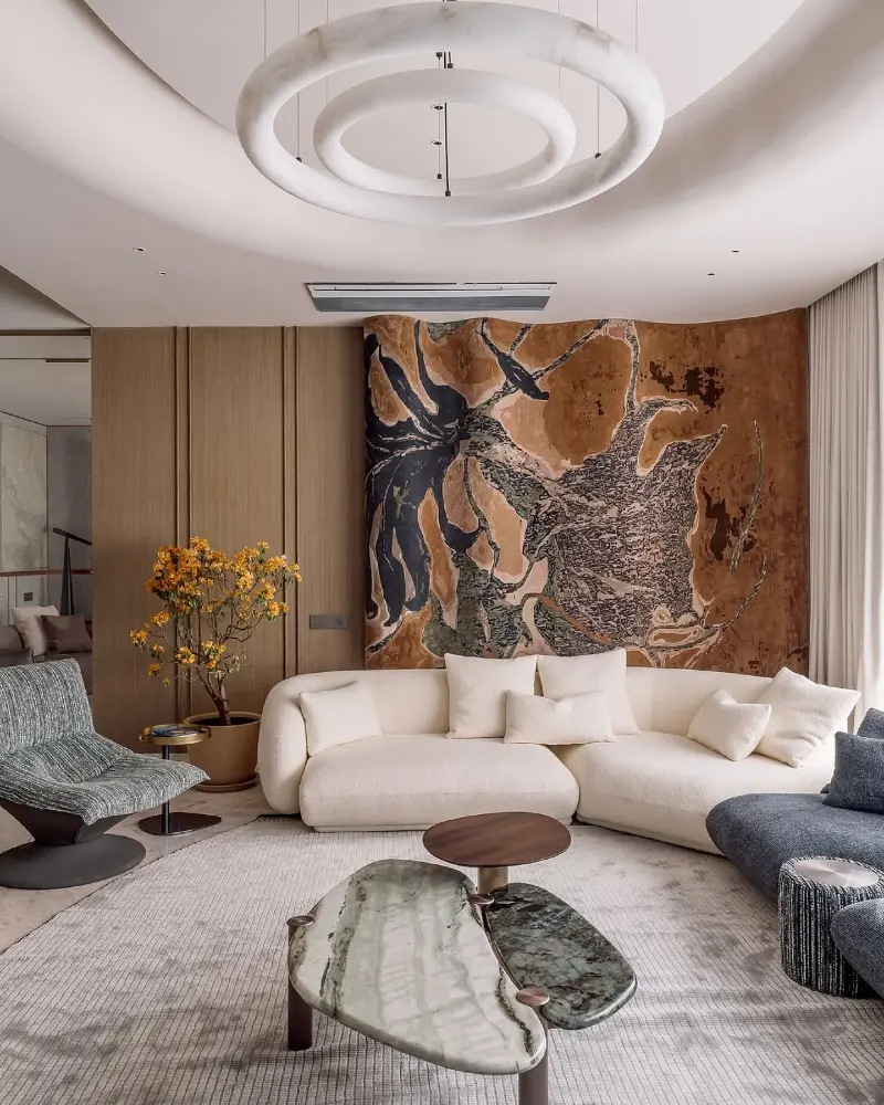 Curved Cream BouclΓ© Sofa with Polished Marble Tables and Abstract Textured Wall Panel
