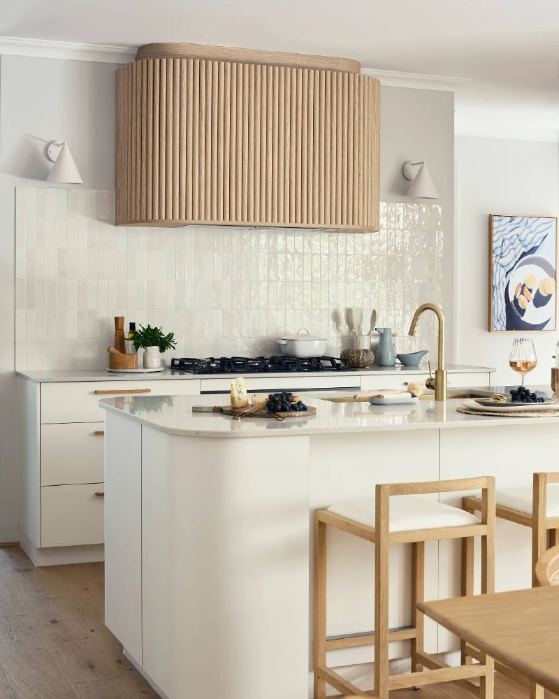 Curved Wood Slat Range Hood with Glossy White Tile Backsplash and Soft Minimal Island Seating