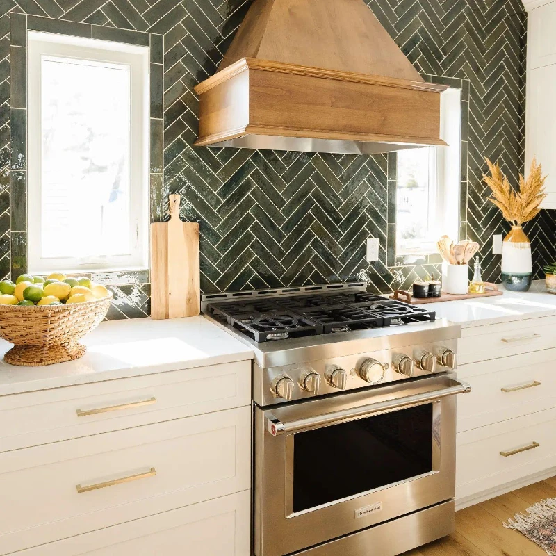 Glossy Forest Green Herringbone Backsplash with Wood Range Hood and Bright Window Light