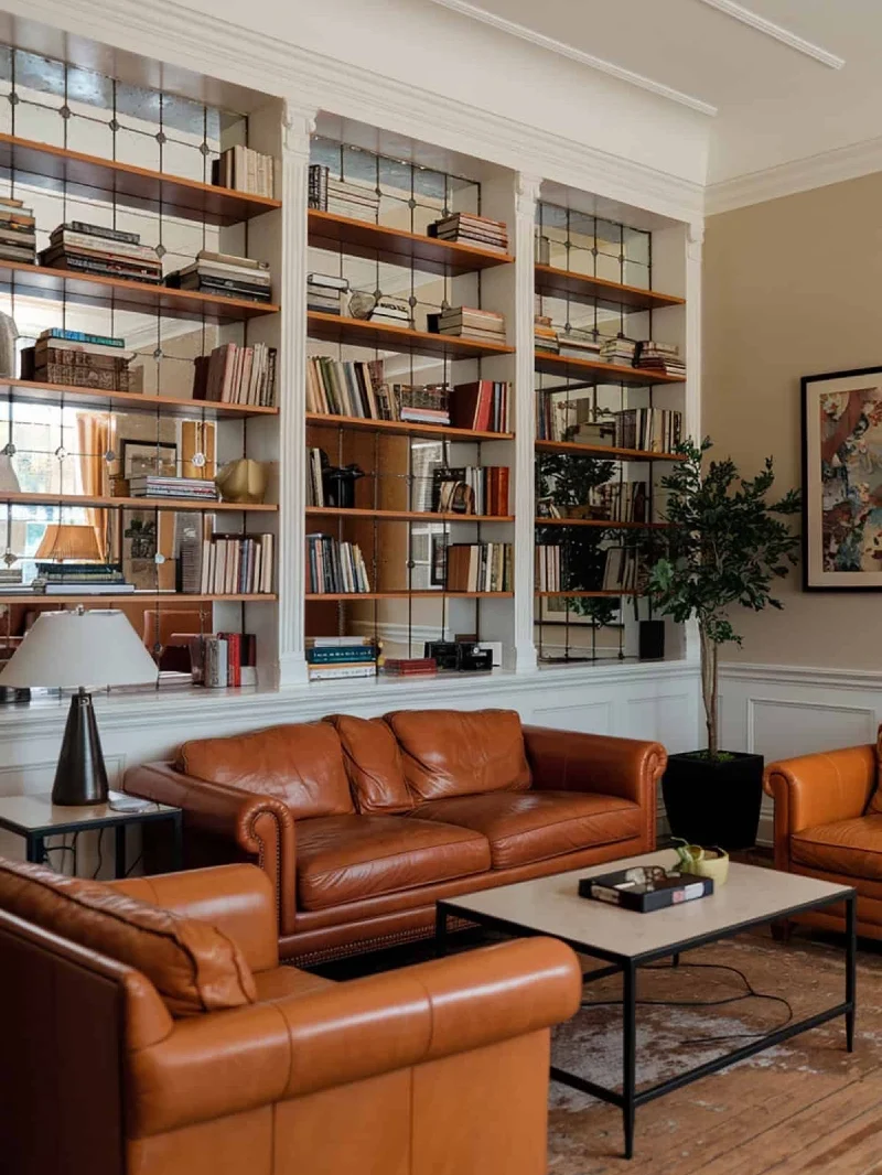 Mirrored Library Wall with Wood Shelves and Caramel Leather Seating