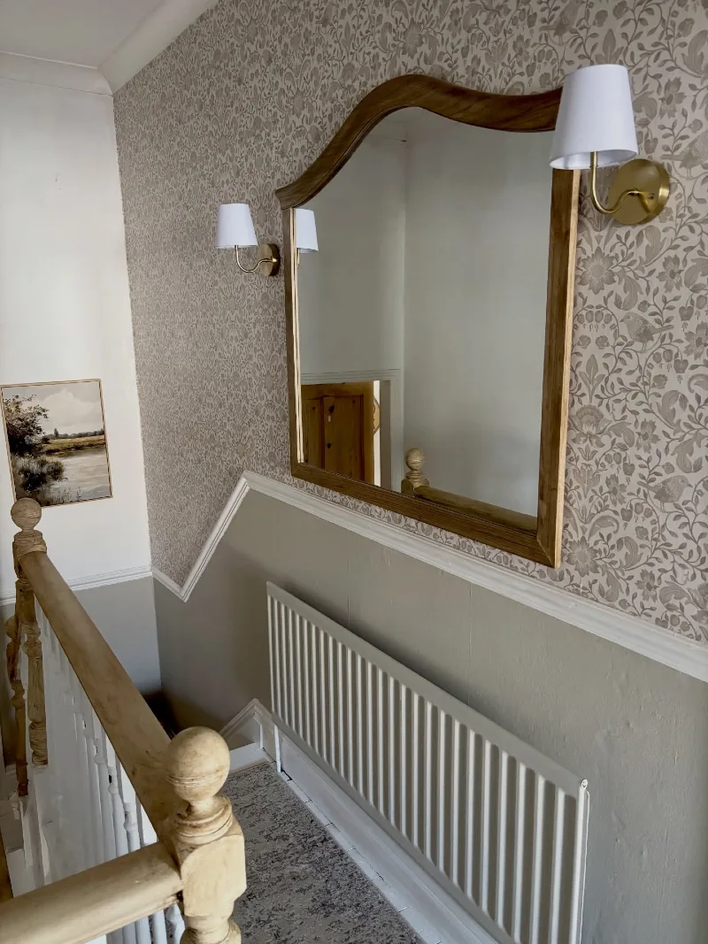 Ornate Wooden Mirror with Brass Sconces on Floral Wallpaper