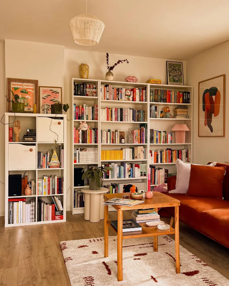 Peach Toned Book Wall with Rust Sofa, Rattan Pendant, and Playful Art