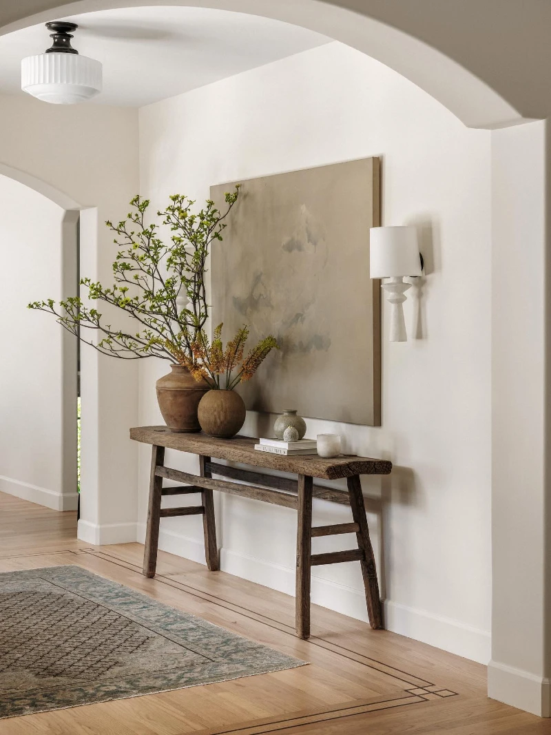 Raw Wood Console Bench with Branchy Greenery, Muted Canvas, and White Wall Sconce