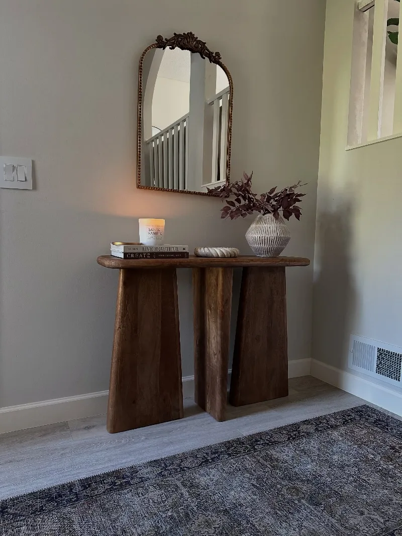 Sculptural Wood Console with Ornate Arched Mirror, Glowing Candle, and Burgundy Branches