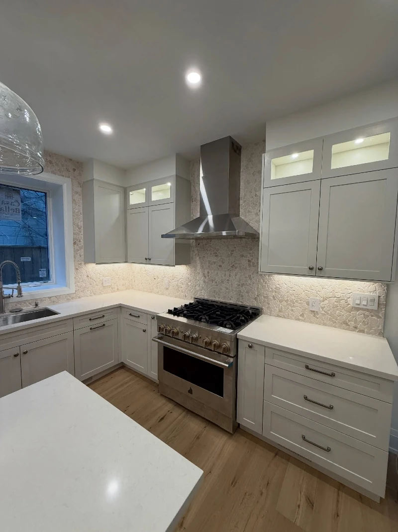 Soft Stone Texture Backsplash with Light Cream Cabinets and Stainless Range Hood