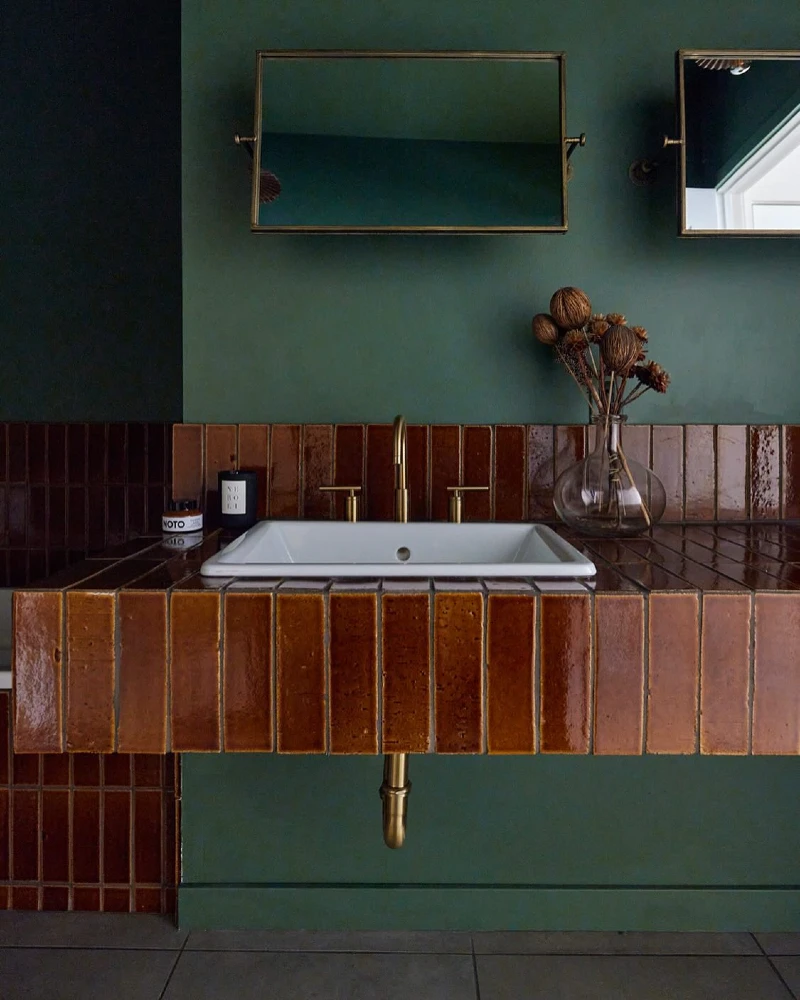 Terracotta Tiled Apron Vanity with Forest Green Walls and Clear Glass Seed Pod Vase