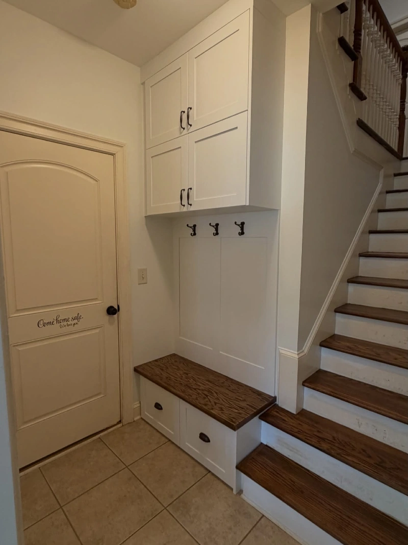 Under-Stairs White Cabinetry with Dark Wood Bench and Black Hooks
