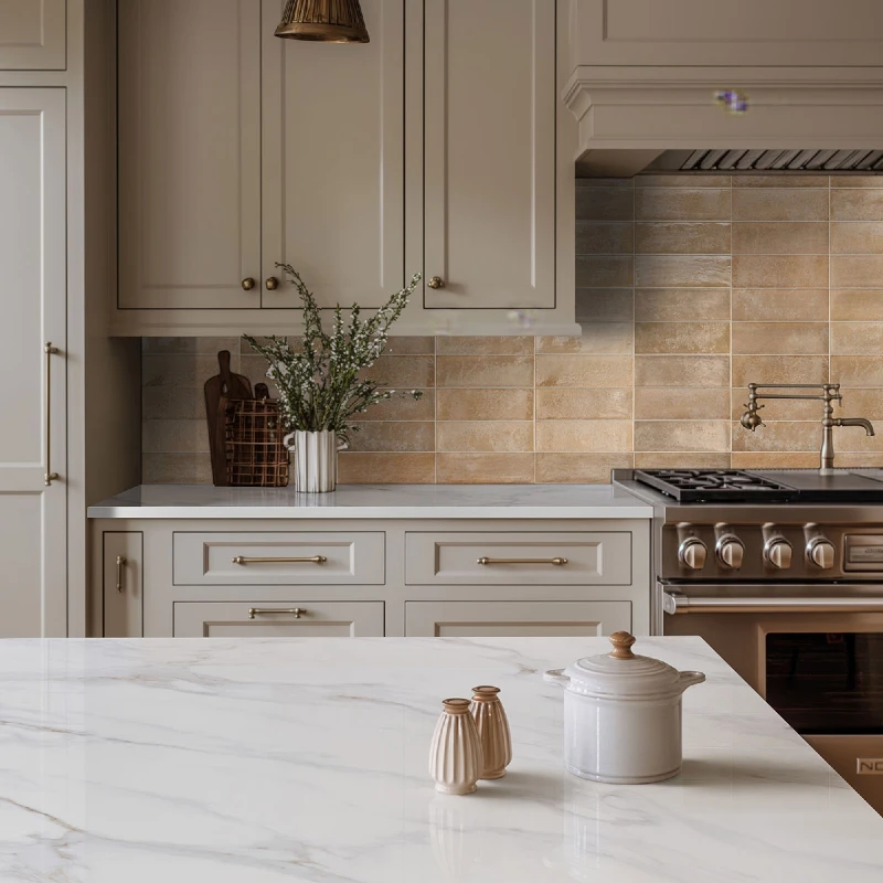 Warm Taupe Subway Tile Backsplash with Soft Cream Cabinets and Brass Range Details