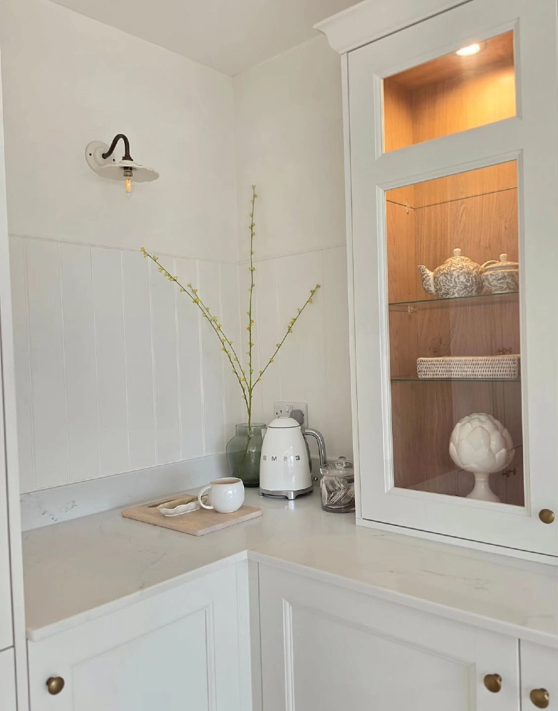 White Beadboard Coffee Corner with Smeg Kettle, Green Glass Vase, and Lit Display Cabinet
