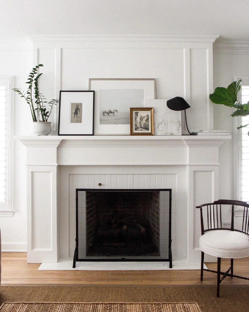 White Paneled Mantel with Leaning Art, Potted Greenery, and a Black Sculptural Lamp