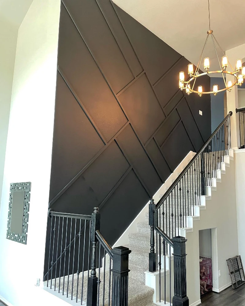 Black Asymmetric Geometric Slat Wall with Gold Hoop Chandelier and Carpeted Staircase