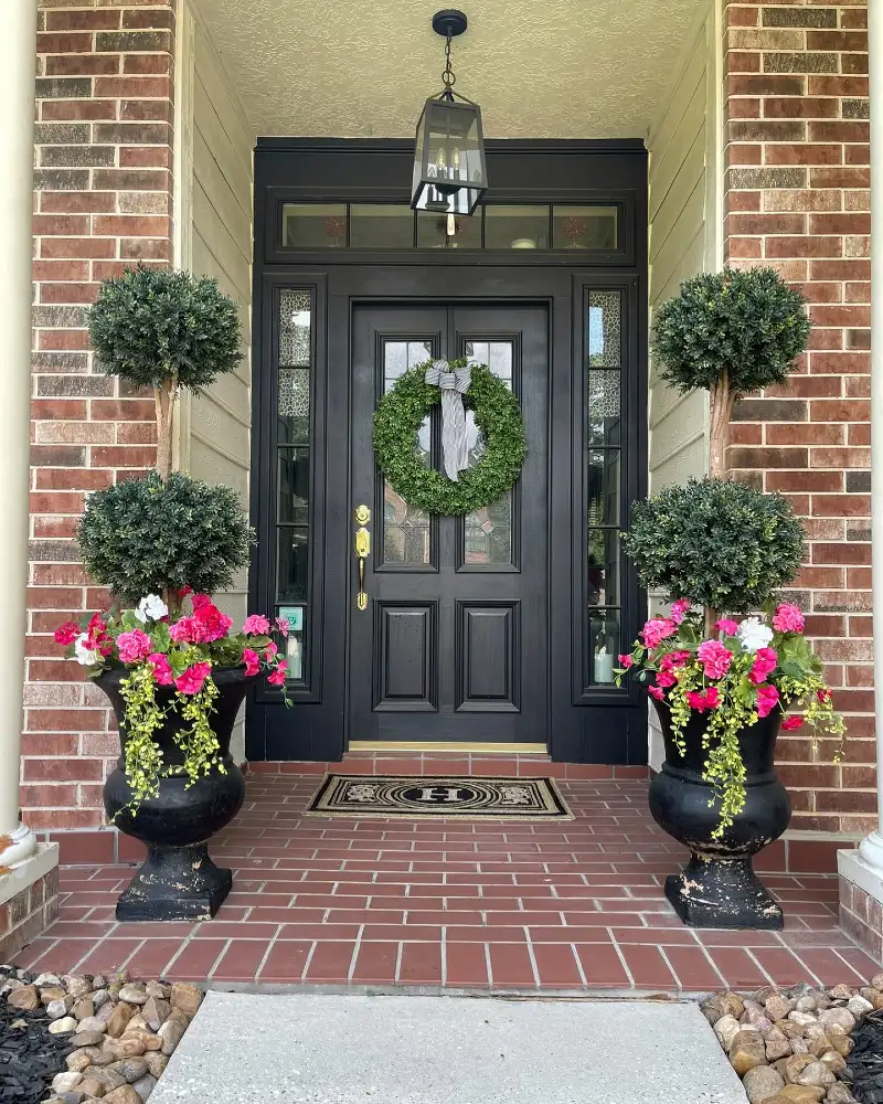Black Paneled Door with Tiered Topiaries and Pink Geranium Urns