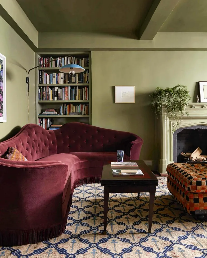 Curved Burgundy Velvet Sofa with Olive Walls and Patterned Ottoman