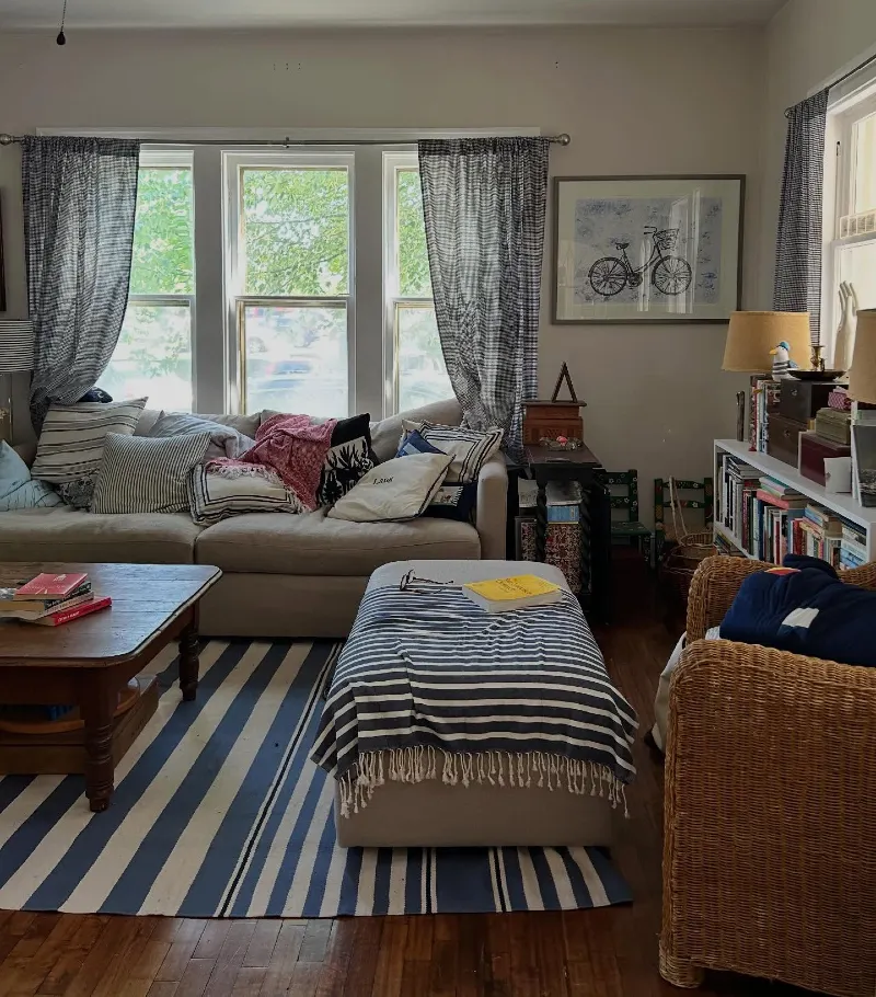 Cushioned Ottoman Bench beside Striped Area Rug and Woven Rattan Armchair