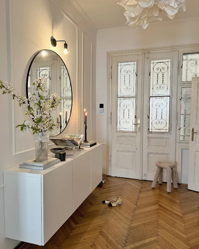 Floating White Credenza with Fluted Glass Vase, Oval Mirror, and Chevron Hardwood Flooring
