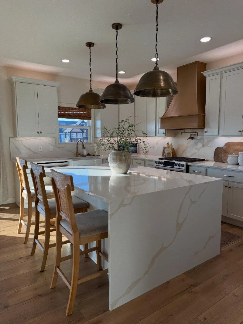 Marble Waterfall Island with Antiqued Brass Pendants and Warm Wood Range Hood