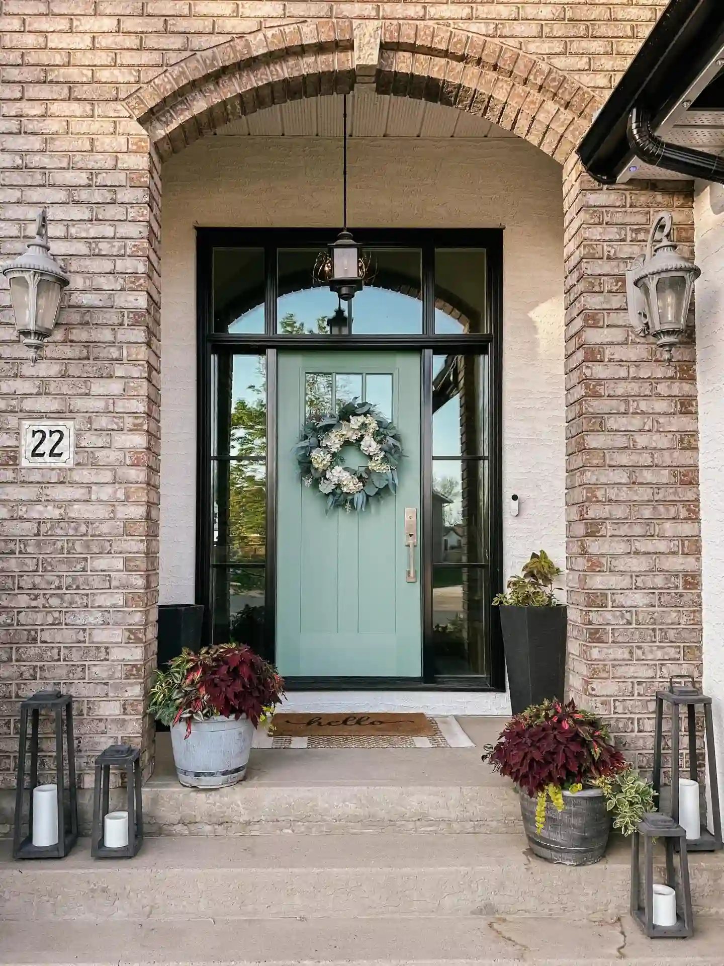Sage Green Door Beneath a Brick Arch with Burgundy Planters