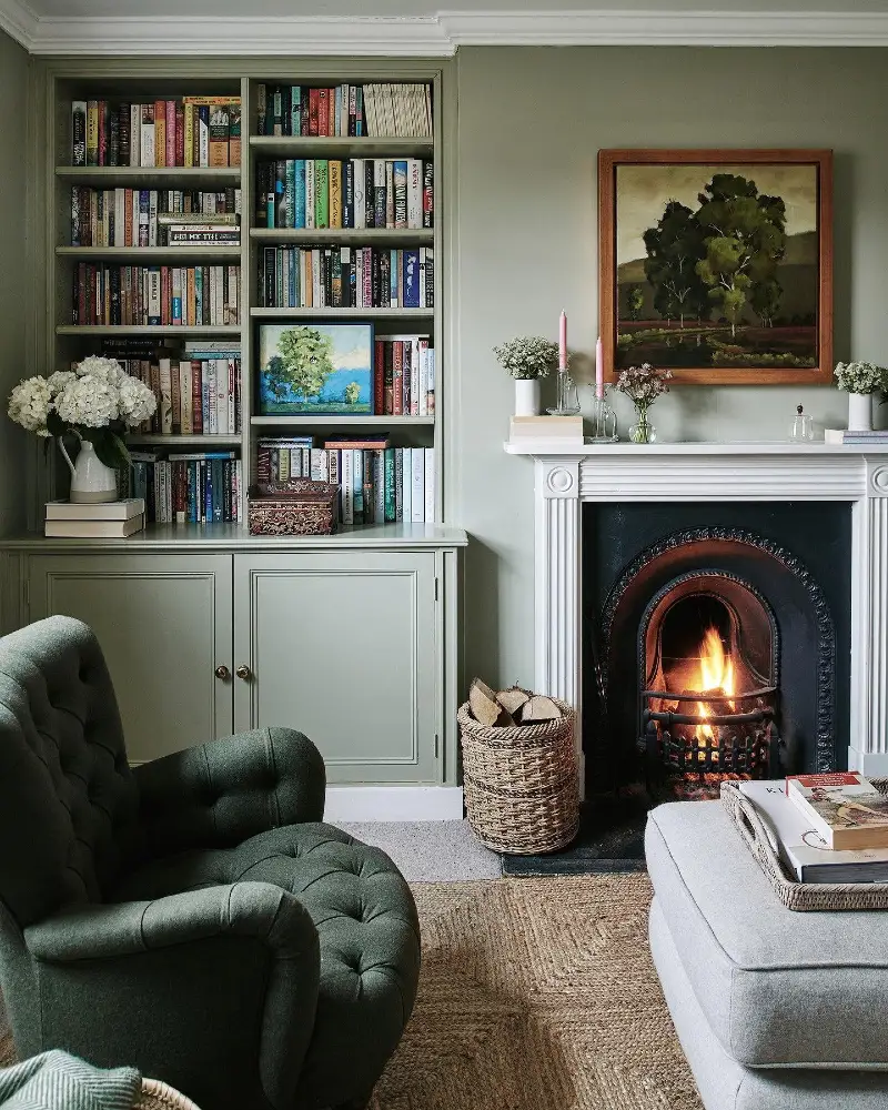 Sage Green Fireplace Nook with Built-In Bookcase, Dark Green Armchair, and Woven Log Basket