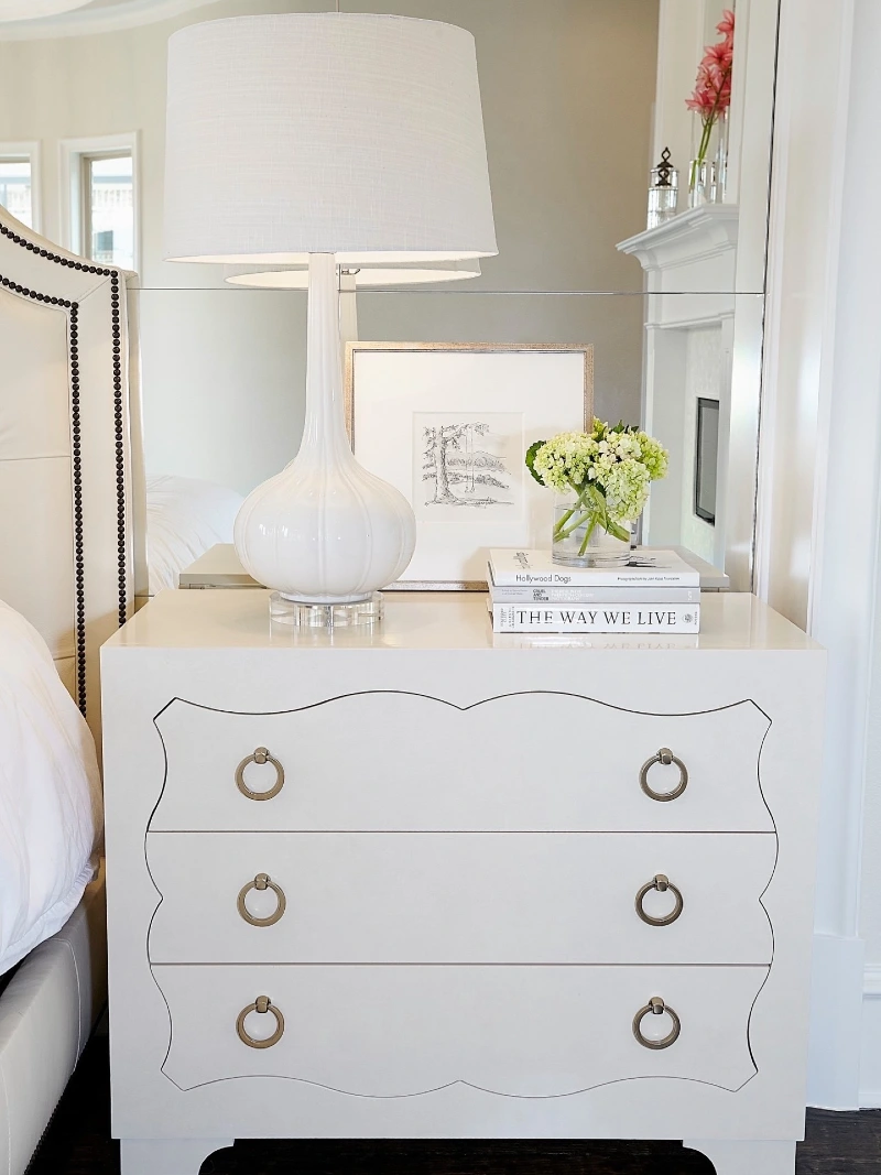 Scalloped Cream Chest with Gourd Lamp and Framed Sketch Against Paneled Mirror