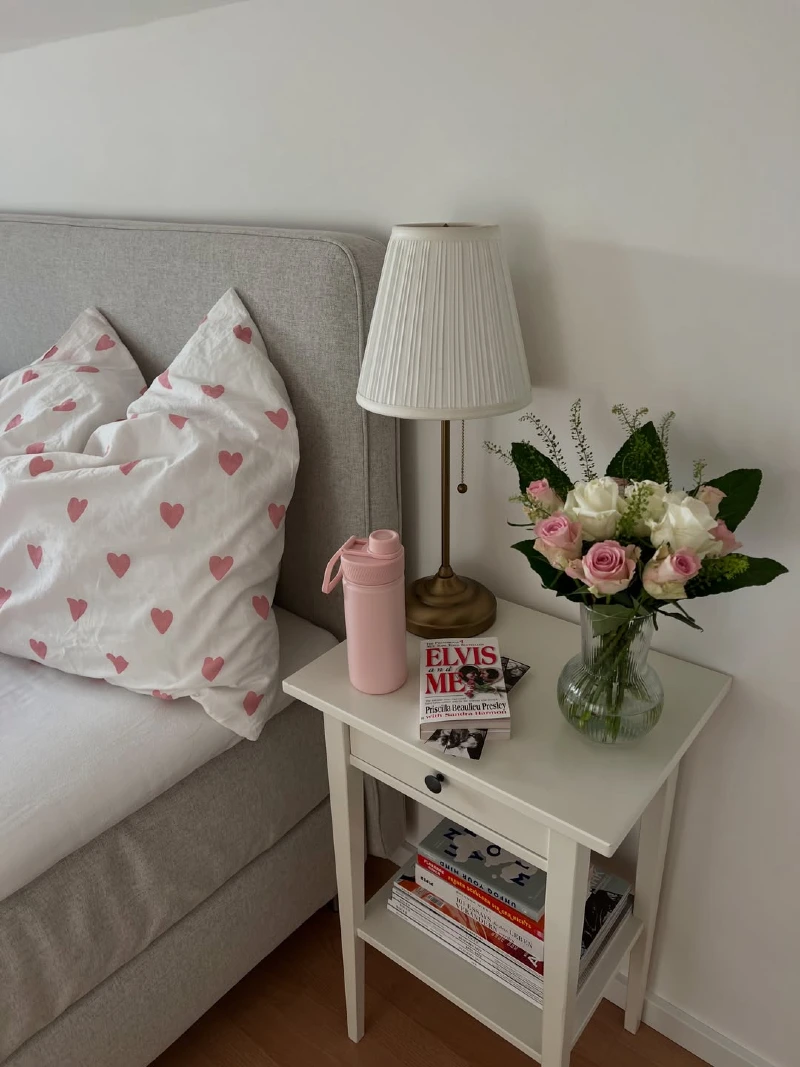 Slender White Nightstand with Pleated Brass Lamp and Pink Heart Pillows