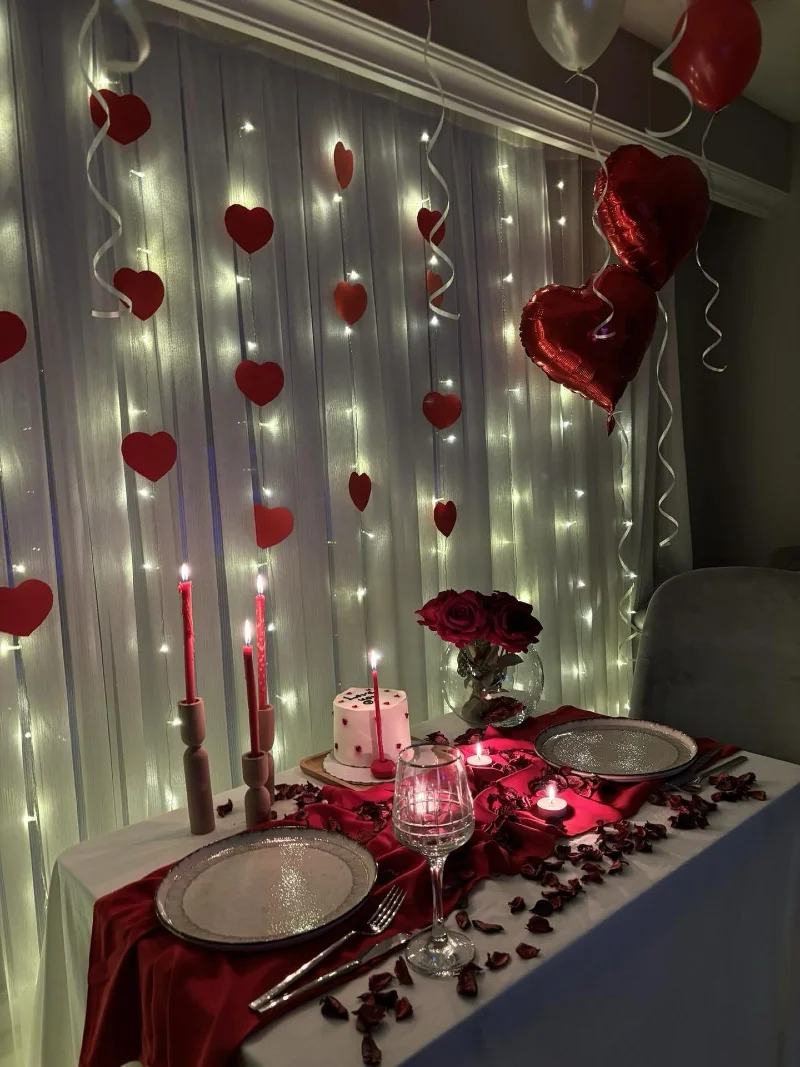 White Backdrop Curtain with Fairy Lights, Red Hearts, and Romantic Dinner Table Setup