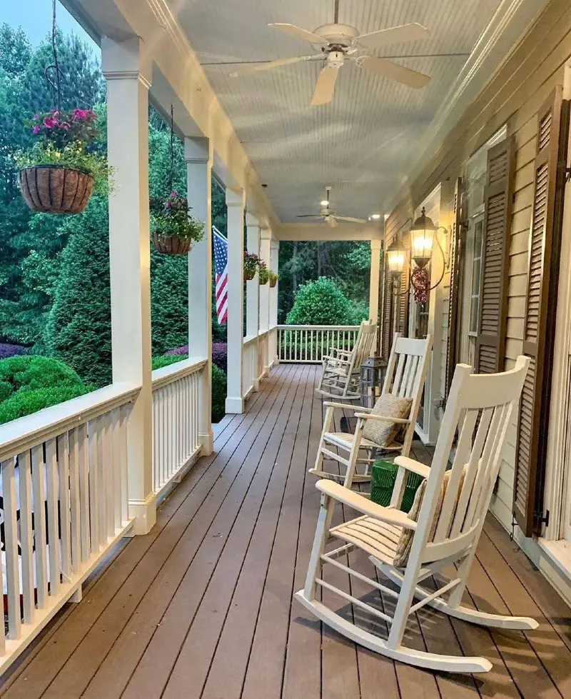 White Rocking Chairs on Wood Deck with Glowing Wall Lanterns and Hanging Baskets