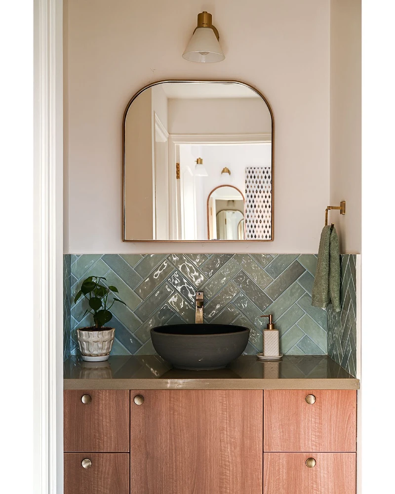Arched Brass-Rimmed Mirror Above Sage Herringbone Tile